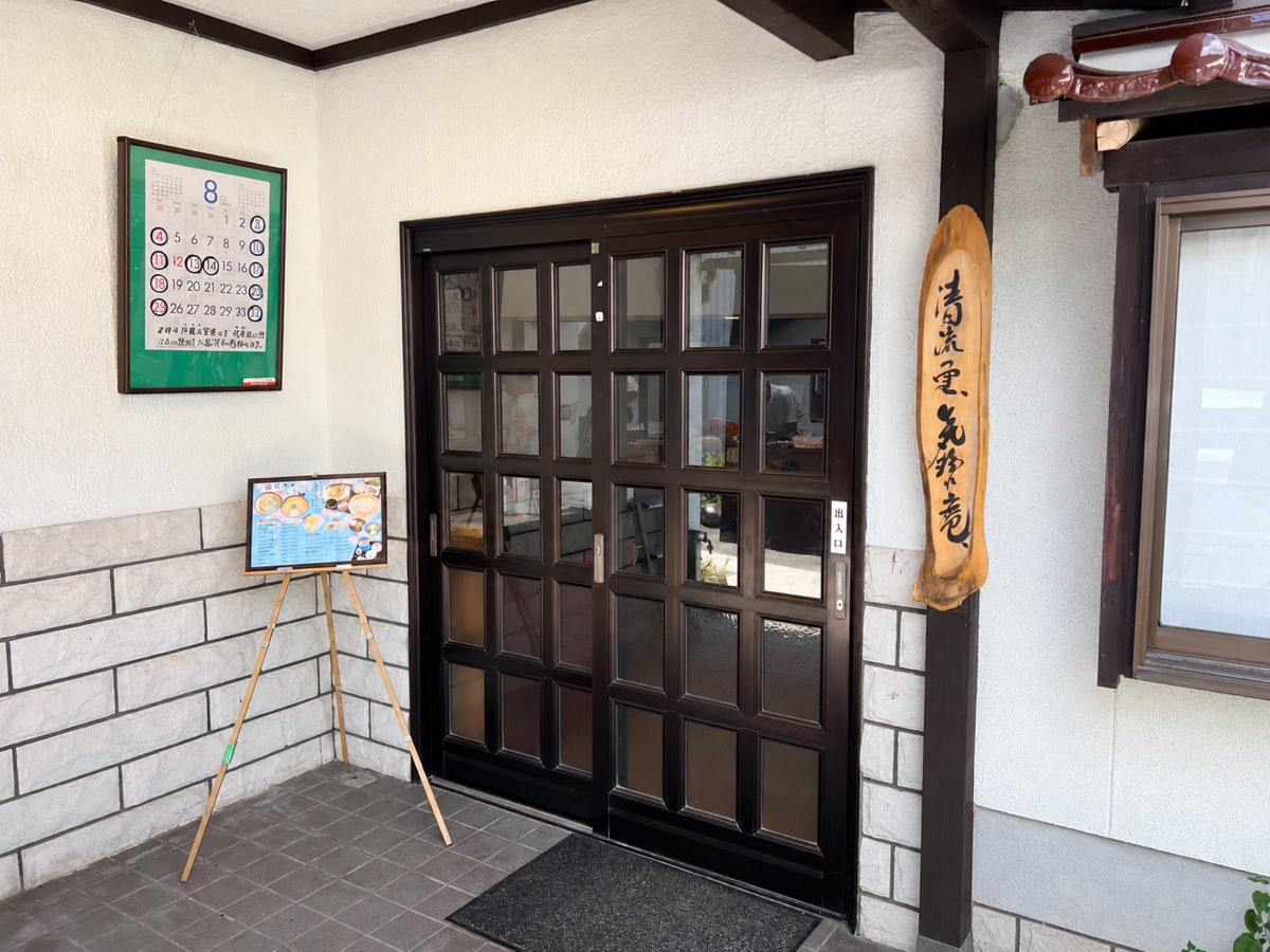 清流の里 気紛れ庵の玄関。木の看板と営業日カレンダー、お品書きの立て看板